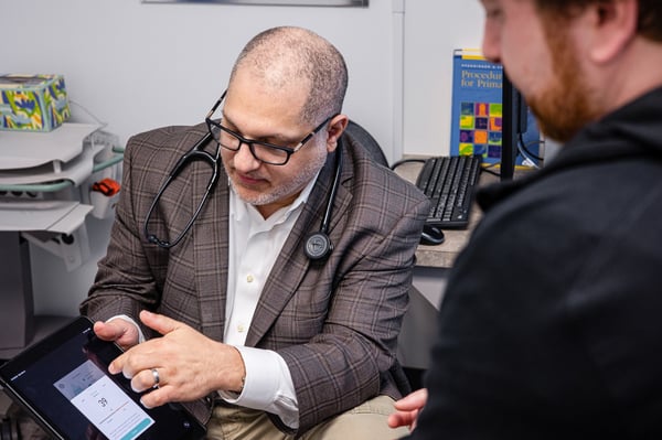 Dr. Wael Aboughali reviews a patient's health information on a tablet during a primary care appointment, explaining results and discussing a personalized care plan.