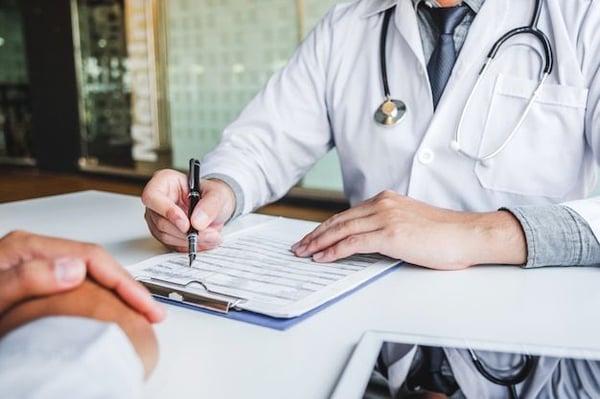 A primary care physician reviews medical information and discusses a personalized treatment plan with a patient during an office consultation.