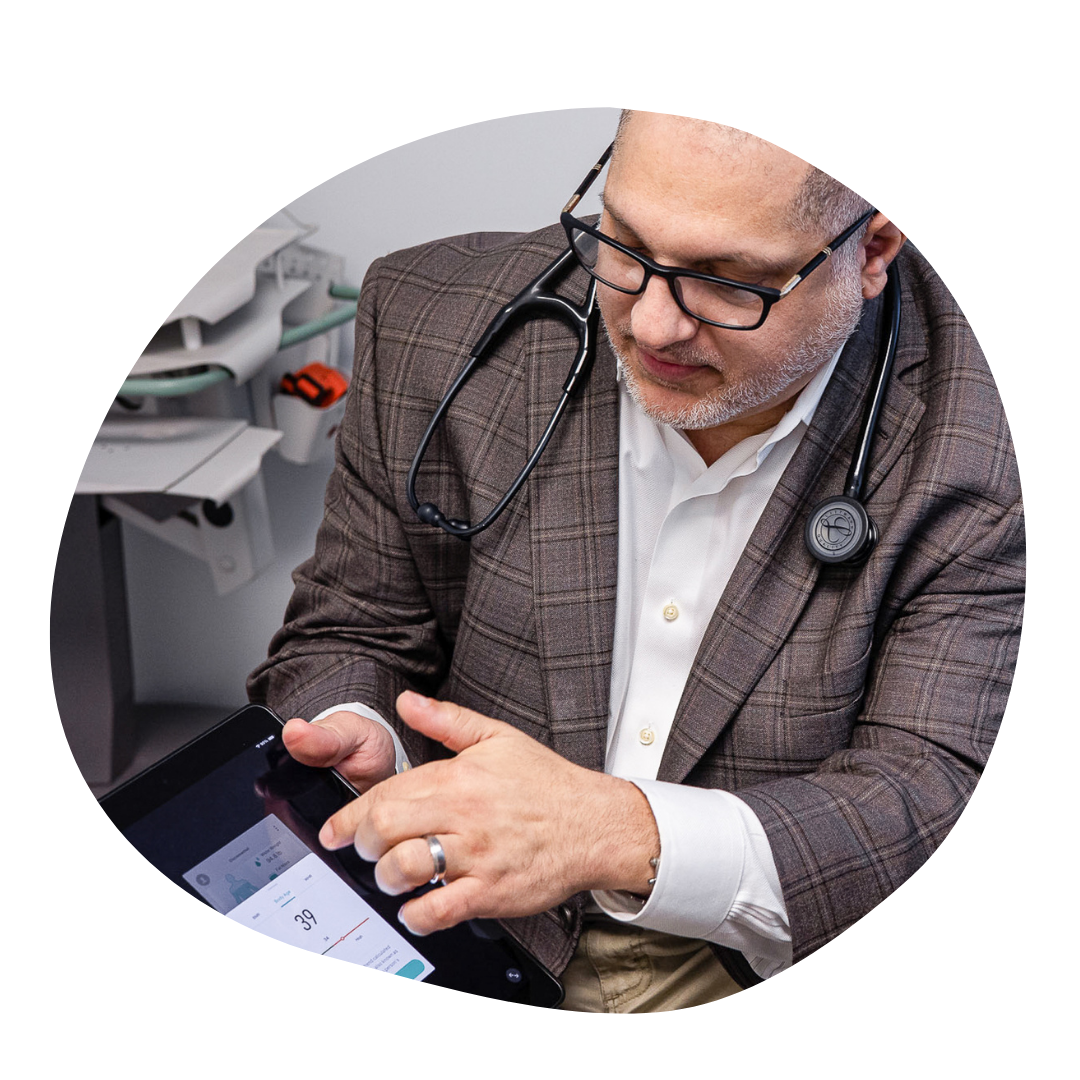 Primary Care Dr. Aboughali with a stethoscope reviews patient health data on a tablet during an appointment at My Doctor Primary Care Clinic.