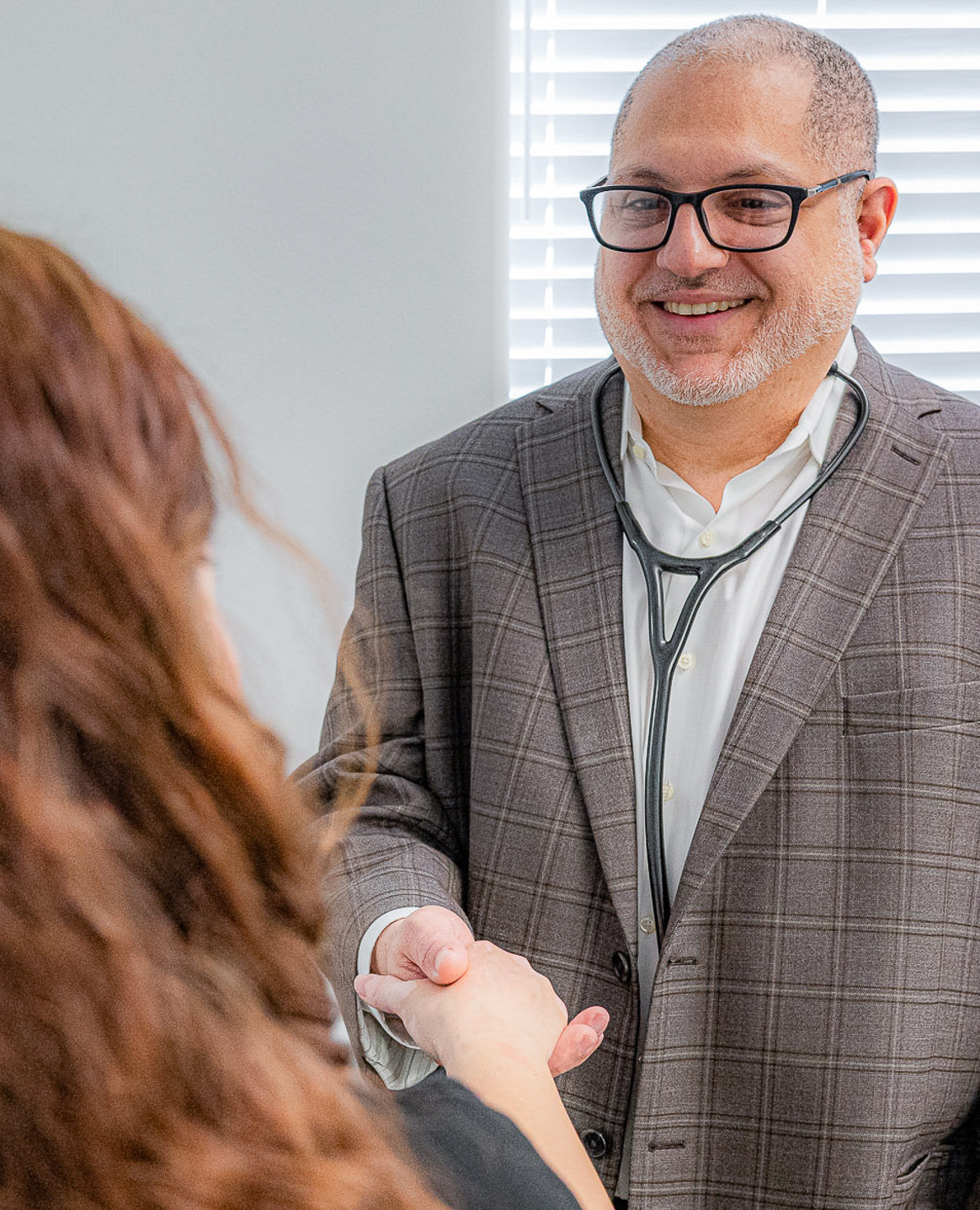 Dr. Aboughali, a primary care physician, warmly greets a patient with a handshake during an office visit, creating a welcoming and personal healthcare experience.