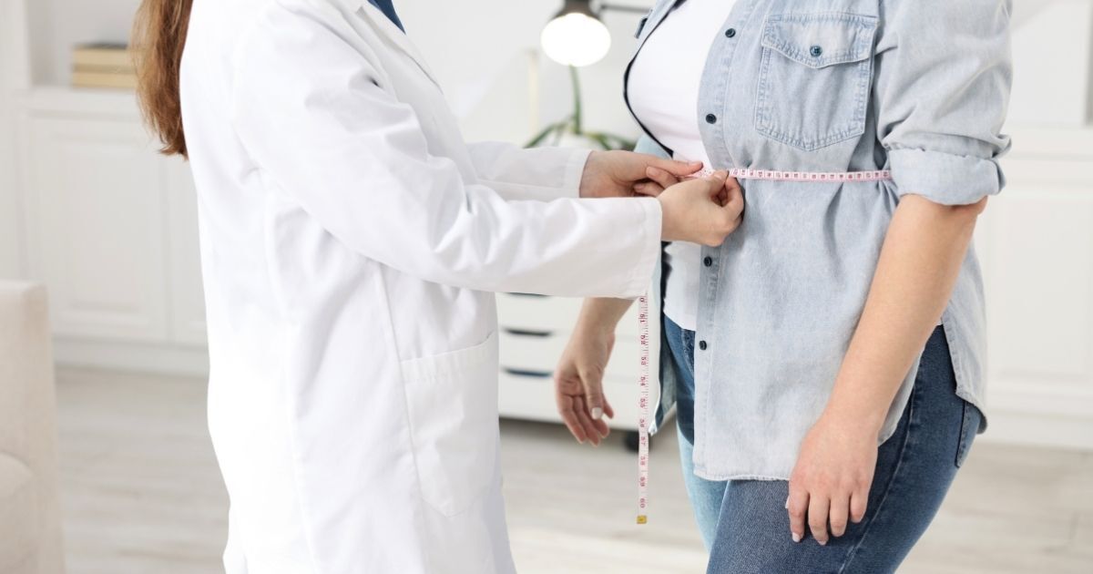 Healthcare professional measuring a patient’s waist with a tape measure during a medical weight management consultation.